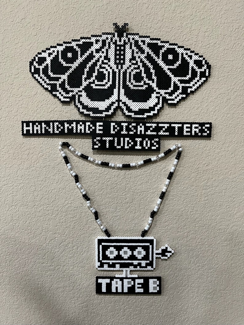 May include: Black and white pixel art of a moth, a necklace with a black and white pixel art cassette tape pendant, and a sign that reads 'HANDMADE DISASTERS STUDIOS' and 'TAPE B'.