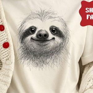 May include: Cream-colored t-shirt featuring a detailed black and white illustration of a smiling sloth's face. The shirt is paired with blue jeans and a cream-colored cardigan. The text "NATURAL COLOR" is visible.