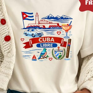 Puede incluir: Camiseta color crema con un gráfico colorido de Cuba. El diseño incluye una bandera cubana, un faro, un coche clásico y las palabras "CUBA LIBRE" en rojo. Otros elementos incluyen un cóctel, un cigarro y un pájaro azul.