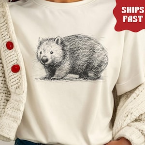 May include: Cream-colored t-shirt featuring a detailed sketch of a wombat. The wombat is depicted in a cross-hatch style, with a focus on texture and shading. The shirt also has the text "NATURAL COLOR".