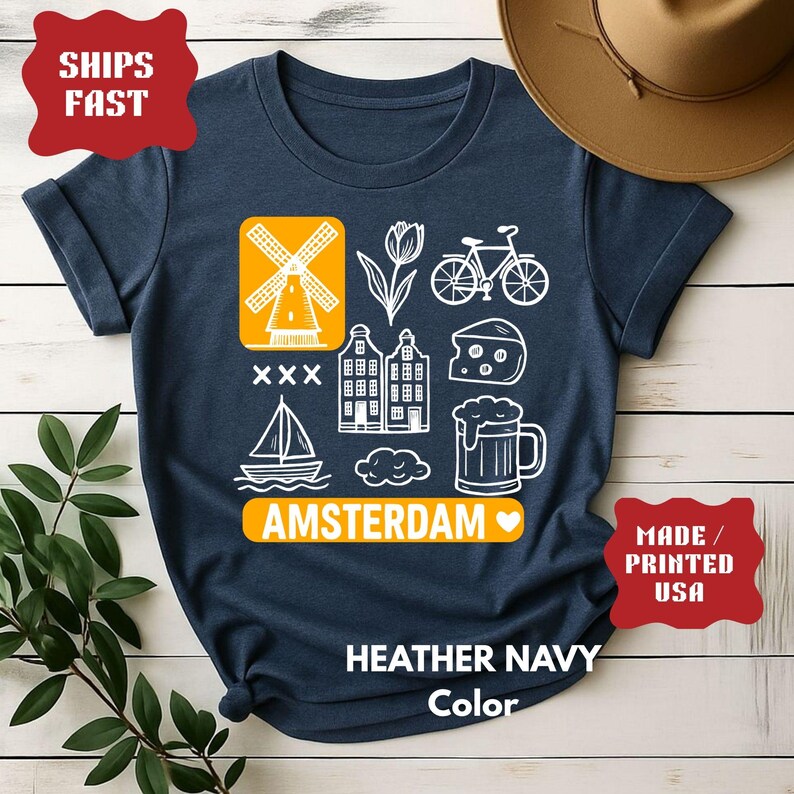 Heather navy t-shirt with white graphic icons of a windmill, tulips, bicycle, houses, cheese, beer, and a sailboat. The word "AMSTERDAM" is in orange.