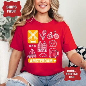 Pu&ograve; includere: T-shirt rossa con icone grafiche bianche: mulino a vento, tulipano, bicicletta, formaggio, edifici, boccale di birra, barca a vela e nuvola. La parola "AMSTERDAM" &egrave; stampata sotto. Prodotto negli Stati Uniti.
