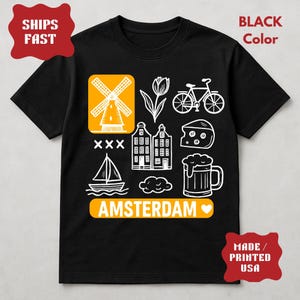 Pu&ograve; includere: T-shirt nero con grafica bianca a tema Amsterdam, tra cui un mulino a vento, un tulipano, una bicicletta, formaggio, case, una barca a vela, un boccale di birra e la scritta "AMSTERDAM". La maglietta ha anche il testo "BLACK Color" e "MADE / PRINTED USA".