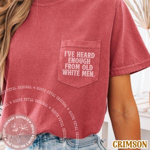 May include: Crimson-colored t-shirt with a pocket featuring the text "I'VE HEARD ENOUGH FROM OLD WHITE MEN." The shirt has a round neck and short sleeves. The words "Rogue Petal Original" are printed around the shirt.