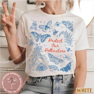 May include: White t-shirt featuring blue illustrations of butterflies, bees, and plants, with the text "Protect Our Pollinators" in red. The design includes stars and floral elements, creating a nature-themed graphic.