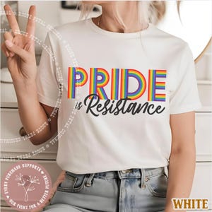 May include: White t-shirt with the text "PRIDE is Resistance" in rainbow colors and black font. The shirt is a crew neck style and is being worn by a person. The words "ROGUE PETAL ORIGINAL" are printed around the shirt.