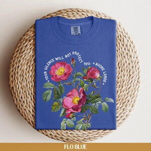 May include: A blue t-shirt with a floral design and the text "Your silence will not protect you. - Audre Lorde".