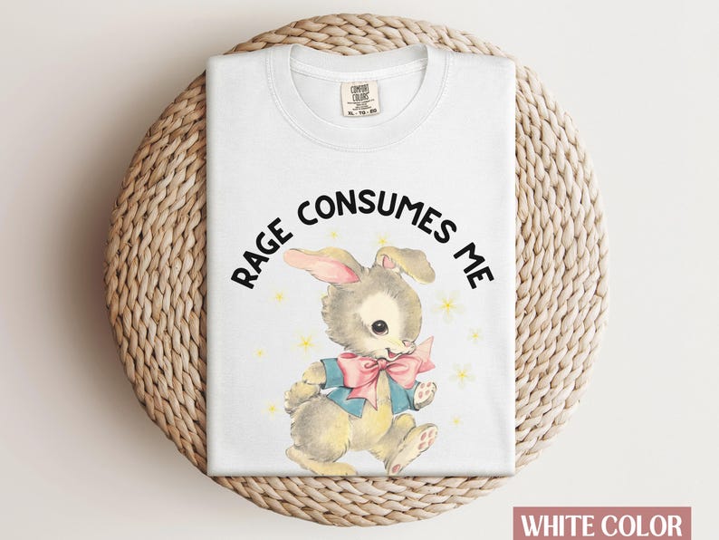 Op de afbeelding: Wit T-shirt met een cartoonkonijn met een blauwe strik en de tekst "RAGE CONSUMES ME".