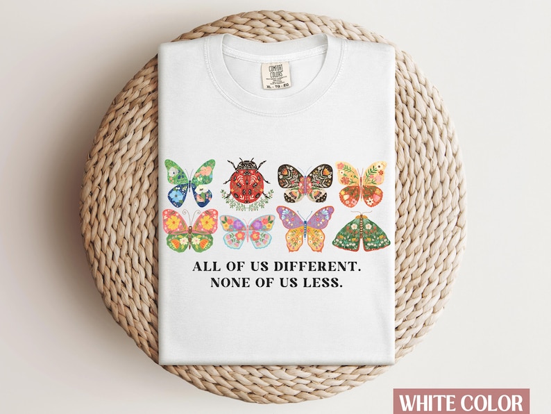 May include: White t-shirt with a graphic of colorful butterflies and a ladybug. The text "All of us different. None of us less." is printed below the graphic.