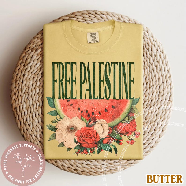 May include: A yellow t-shirt with the text "FREE PALESTINE" in green, above a watermelon slice and floral arrangement. The shirt is folded on a woven surface. The word "BUTTER" is at the bottom right.