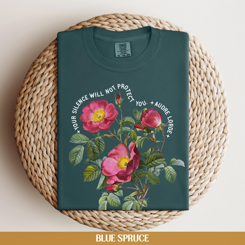 May include: A teal blue t-shirt with a floral design and the text "Your silence will not protect you. - Audre Lorde".