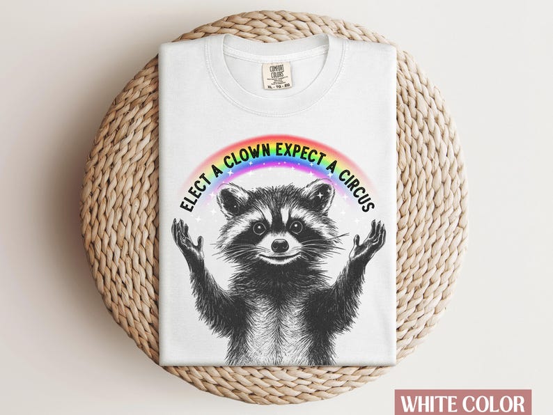 May include: White t-shirt with a raccoon wearing a rainbow and the text "Elect a clown expect a circus".