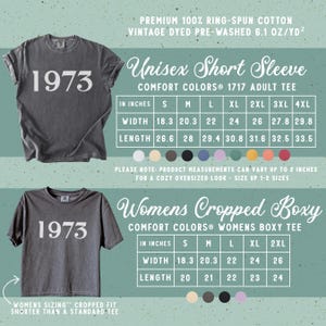 May include: A charcoal grey t-shirt with the text 1973 in white. The image includes two sizing charts for a short sleeve tee and a cropped boxy tee, listing widths and lengths in inches for sizes S through 4XL, made of 100% ring-spun cotton.