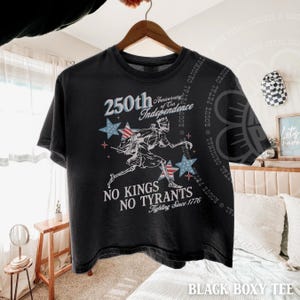 May include: Black boxy tee shirt with a graphic celebrating the 250th anniversary of independence. The design includes stars, a running figure, and the text "No Kings No Tyrants Fighting Since 1776."