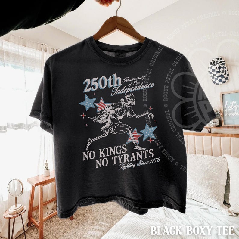 May include: Black boxy tee shirt with a graphic celebrating the 250th anniversary of independence. The design includes stars, a running figure, and the text "No Kings No Tyrants Fighting Since 1776."