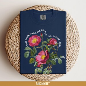 May include: A navy blue t-shirt with a floral design and the text "Your silence will not protect you. - Audre Lorde".