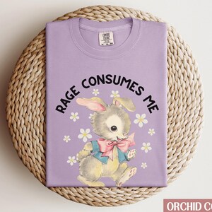 Op de afbeelding: Een paars T-shirt met een cartoonkonijn en de tekst "Rage Consumes Me" erop gedrukt.