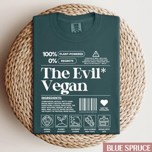May include: A dark green t-shirt featuring a white graphic that reads "The Evil* Vegan" with a plant-powered and zero regrets message. The graphic also includes a barcode, a heart with the text "For the voiceless", and icons representing animal lover, planet activist, gourmet foodie, half human half tofu, and vegan spot GPS.