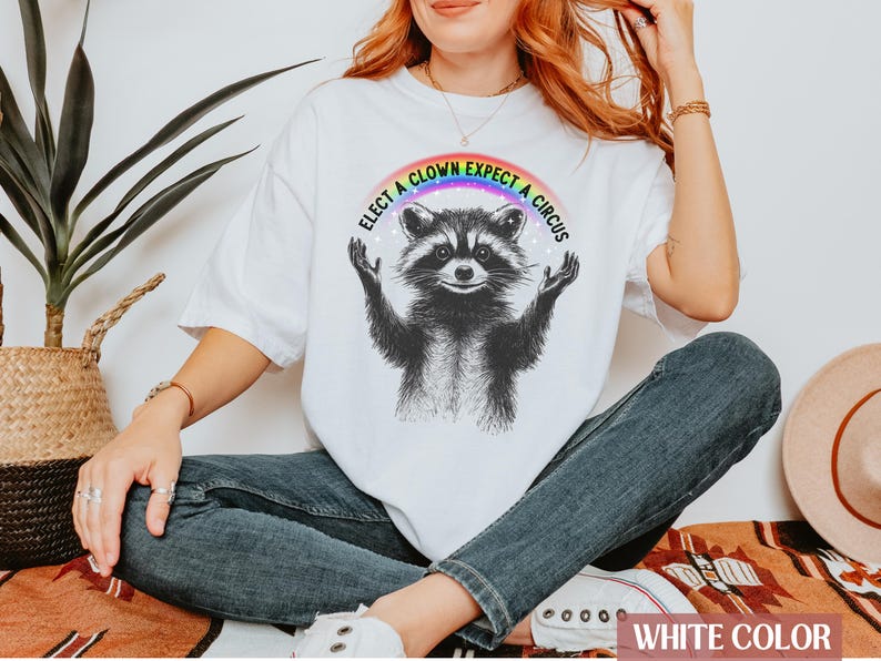 May include: White t-shirt with a rainbow and the text "Elect a Clown Expect a Circus" above a black and white illustration of a raccoon.