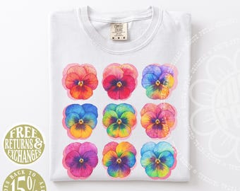 Puede incluir: Una camiseta blanca con una cuadrícula de nueve flores de pensamiento estilo acuarela en varios colores vibrantes, incluyendo naranja, rojo, azul, amarillo y morado. La camiseta tiene una etiqueta de la marca Comfort Colors en el cuello y es talla M.