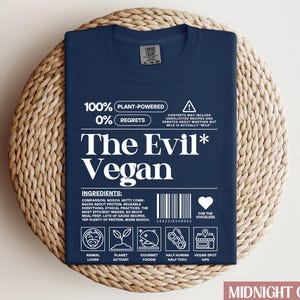 May include: A navy blue t-shirt with white text that reads "100% Plant-Powered 0% Regrets The Evil* Vegan". The shirt has a barcode and a heart with the text "For the Voiceless".