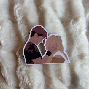 May include: A sticker depicting a couple in a close embrace. The man has dark hair and a black shirt with a red pattern. The woman has blonde hair and is being held by the man. The sticker has a white border.