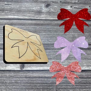 May include: Wooden die-cut bow shape with the text "WQ001" and three glittery bows in red, lavender, and rose colors. The bows are on a gray wooden surface.