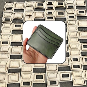 May include: A dark olive green leather card holder featuring three horizontal slots for cards and visible stitching along the edges. The card holder is displayed against a background of numerous wooden cutting dies used for leather crafting.
