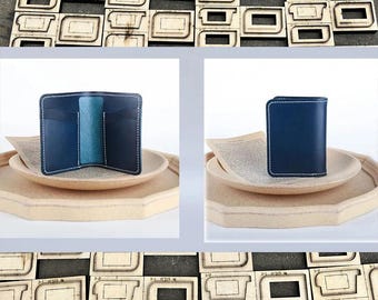 May include: A handmade blue leather wallet with white stitching, displayed open and closed on a wooden tray. The wallet has multiple card slots and a central compartment. The image also shows wooden cutting dies.