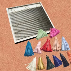 May include: A metal tassel maker with a series of parallel grooves and several colorful leather tassels. Tassels are in various colors, including blue, pink, red, green, and gold. The tassels are made of leather.