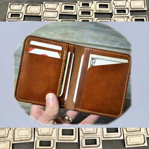 May include: Open brown leather wallet with multiple card slots and a bill compartment. The wallet is held open, revealing cards and a bill. The edges are stitched with a contrasting thread.