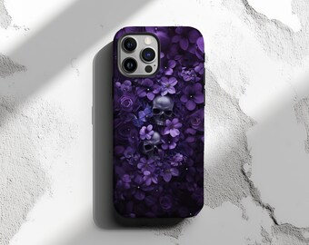 Puede incluir: Carcasa de teléfono púrpura y negra con un diseño floral y calaveras. La carcasa tiene una protuberancia de cámara elevada y un borde negro.