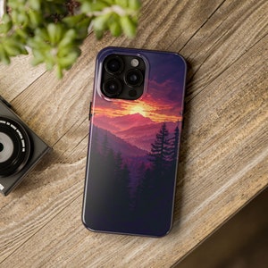 Op de afbeelding: Een telefoonhoesje met een zonsondergang boven een bergketen met bomen op de voorgrond. Het hoesje heeft een zwarte achtergrond en een paarse, roze en oranje zonsondergang.