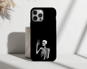 Puede incluir: Funda de teléfono negra con un diseño de esqueleto blanco haciéndose un selfie. El esqueleto sostiene un smartphone, con la caja torácica y el cráneo visibles. La funda tiene un acabado brillante y un recorte para la cámara.