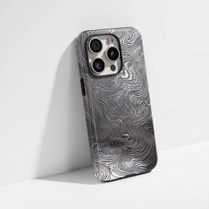 May include: A smartphone case with a swirling, metallic pattern in shades of grey and silver. The case has a glossy finish and features a camera module with multiple lenses. The design resembles a damascus steel effect.