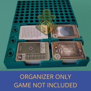 May include: A teal game organiser with the text "FIELDS OF FIRE" and "ORGANIZER ONLY GAME NOT INCLUDED". The organiser holds game cards and components. The box top is green with the game title.