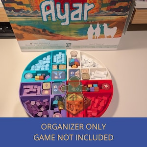 Op de afbeelding: Een veelkleurige organizer voor bordspellen met compartimenten gevuld met spelstukken. De organizer is verdeeld in secties van blauw, paars, rood en wit. De speldoos, getiteld "Ayar", is zichtbaar op de achtergrond. Tekst op de afbeelding luidt "ALLEEN ORGANIZER SPEL NIET INBEGREPEN."