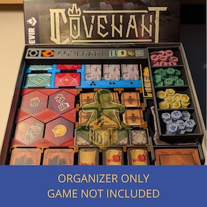 Könnte beinhalten: Ein schwarzer Brettspiel-Organizer für das Spiel "Covenant". Er enthält Fächer für Spielteile wie Karten, Spielsteine und Würfel. Die Spielteile sind in verschiedenen Farben wie Rot, Blau, Grün und Gelb gehalten. Der Text "ORGANIZER ONLY GAME NOT INCLUDED" steht unten.