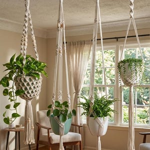 May include: Four macrame plant hangers with various green plants suspended from the ceiling. The hangers are made of off-white rope and feature wooden beads. The plants are in different colored pots, including white and teal, adding a touch of color to the room.
