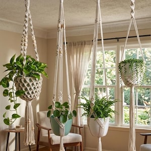 May include: Four macrame plant hangers suspended from the ceiling, each holding a different potted plant. The hangers are made of off-white rope with wooden beads. The plants include a pothos, a fern, and a trailing succulent. The room has a neutral color palette.