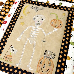 May include: A beige fabric panel with an embroidered skeleton, a cat sitting in a pumpkin, a pumpkin with a face, a bat, stars, and the words "eek!" on a flag. The panel is surrounded by a black and white polka dot fabric border.