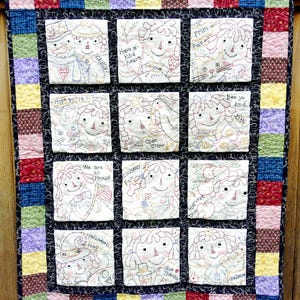 May include: A handmade quilt with a patchwork border in various colors. The quilt features embroidered squares with whimsical characters and phrases like "Chilly," "Have a kind heart," and "Halloween Hag." The overall design is charming and folk-art inspired.