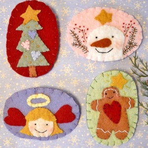 May include: Four felt Christmas ornaments, each with a different design: a green Christmas tree with pink hearts, a pink snowman with a carrot nose, a gingerbread person with a red heart, and a blue angel with red wings.