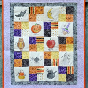 May include: A colourful patchwork quilt with a Halloween theme. Each square features a different Halloween-themed image, such as a bat, pumpkin, owl, witch, apple, spider, ghost, cat, candy corn, and moon. The quilt is made with a variety of fabrics in orange, black, purple, yellow, and white.