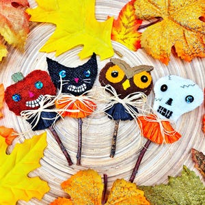 May include: Four Halloween-themed felt figures on sticks. A pumpkin, a black cat, an owl, and a skull. Each figure has googly eyes and a festive orange and black skirt.