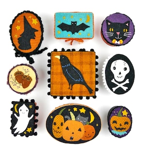 Pode incluir: Nove enfeites de feltro para o Halloween com vários desenhos, incluindo uma bruxa, um morcego, um gato, um corvo, uma caveira e ossos cruzados, um fantasma, uma abóbora e duas bolotas. Os enfeites são todos em tons de preto, branco, laranja e marrom.
