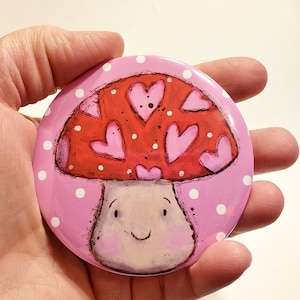 May include: A pink and white polka dot background with a red mushroom with pink hearts on top. The mushroom has a white stem and a smiling face.