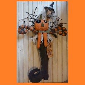 Pode incluir: Uma decoração de Halloween feita à mão com uma boneca com cara de abóbora, uma bota preta e um chapéu de bruxa. A boneca é adornada com tecido laranja e marrom e tem uma etiqueta que diz "One Trick Treat".