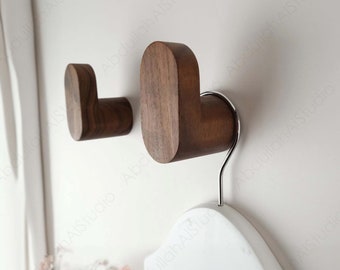 May include: Two wooden wall hooks with a rounded, heart-shaped design. The hooks are made of dark brown wood and are mounted on a white wall. A white hanger is hanging on one of the hooks.