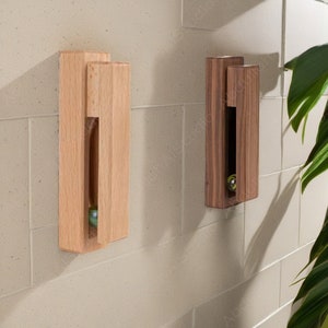 May include: Two wooden wall mounted marble catchers. One is light brown wood and the other is dark brown wood. Each has a small marble inside.